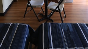 Une pièce de taille modeste, comprenant une petite table ronde, deux chaises blanches, un téléviseur fixé au mur, un four à micro-ondes et un réfrigérateur.