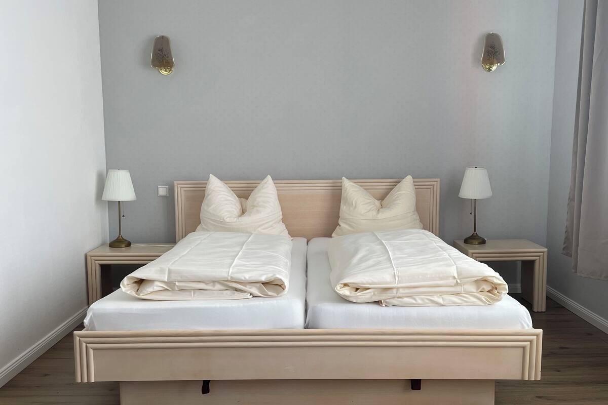 Ein Doppelbett mit hölzernem Kopfteil, zwei Nachttische mit Lampen und hell gestrichene Wände.