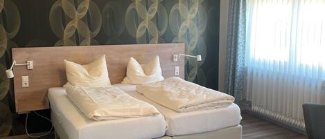 A double bed with white bedding, a wooden headboard, and a wall with a geometric pattern.