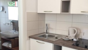 A modern kitchen with white cabinets, a stainless steel sink, and a countertop with a kettle and a coffee maker. - Hotel Markgräfler Hof (Badenweiler)