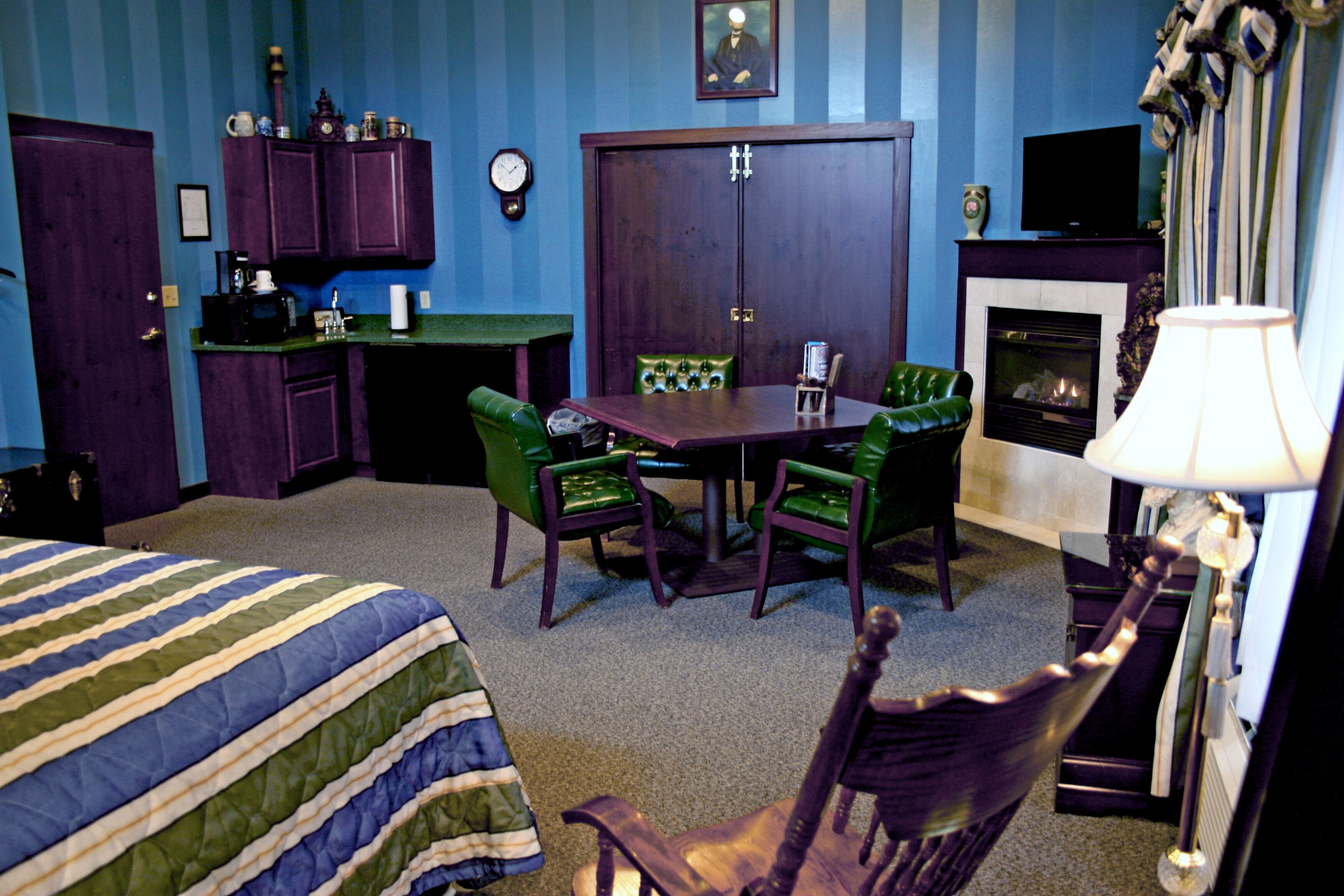 Une chambre d’hôtel avec un lit, une table à manger et des chaises, une cheminée, un téléviseur et une horloge au mur.