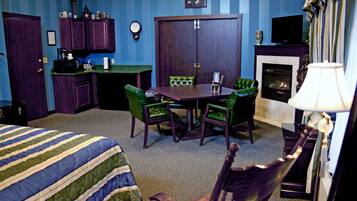 Une chambre d’hôtel avec un lit, une table à manger et des chaises, une cheminée, un téléviseur et une horloge au mur.