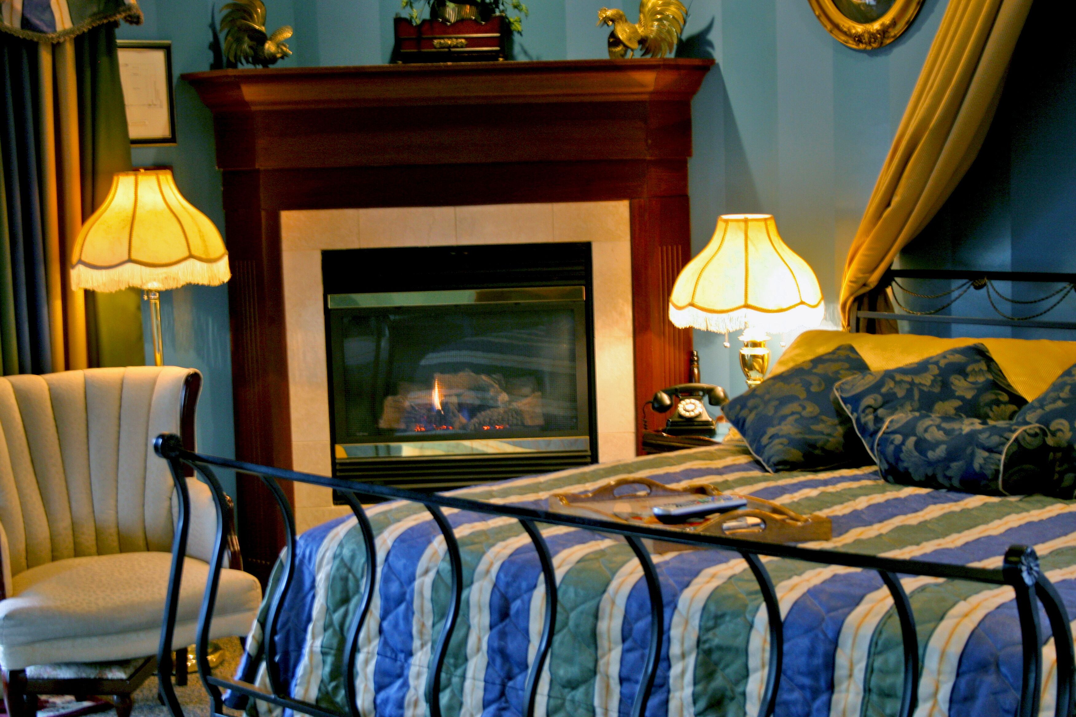 A bedroom with a bed, a chair, a fireplace, and lamps.
