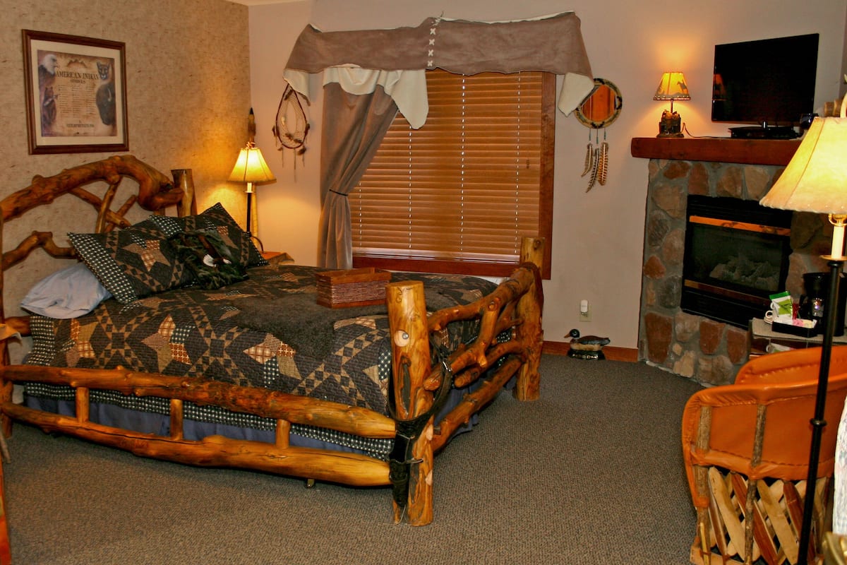 A rustic bedroom with a wooden bed, a stone fireplace, and a television.
