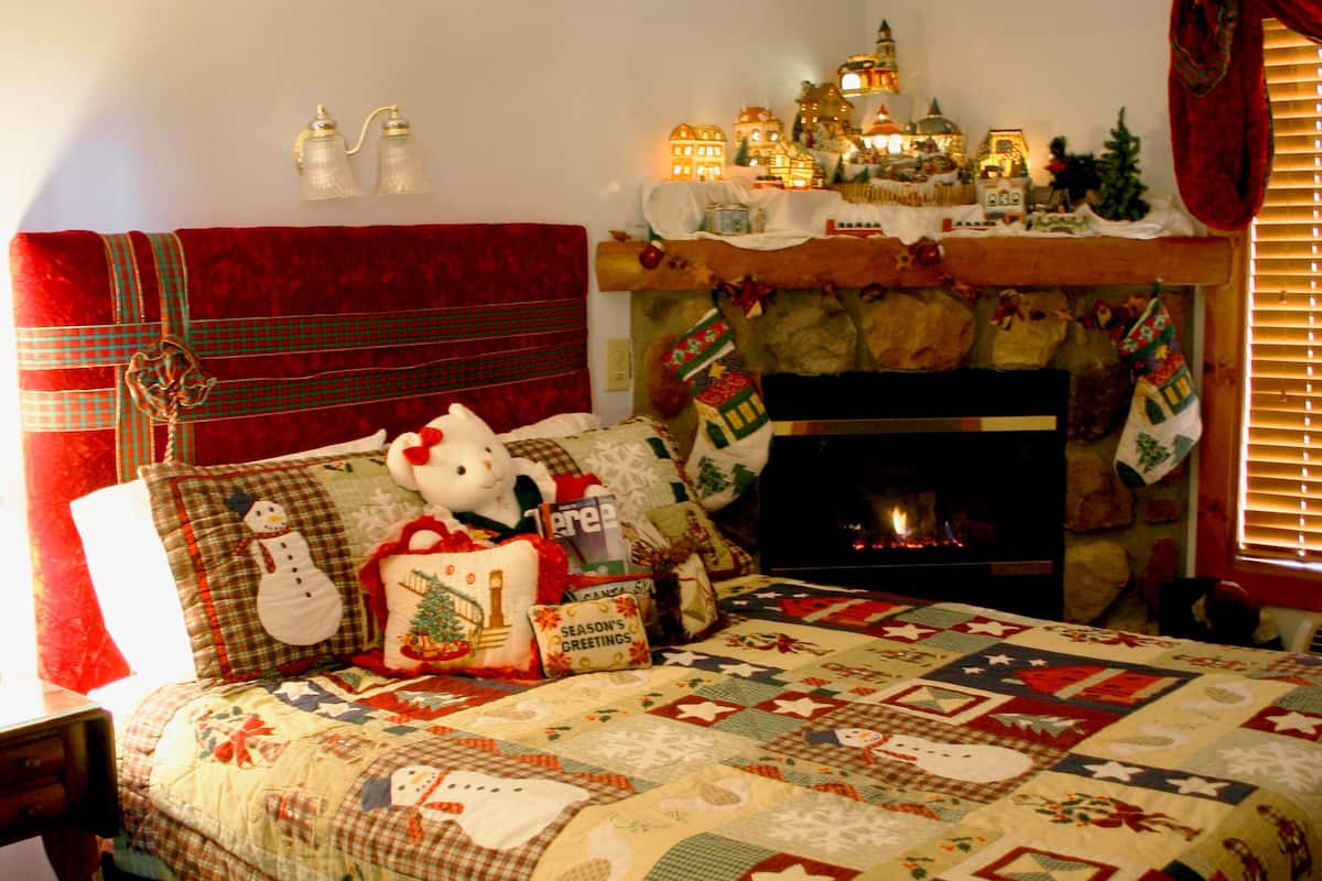 A cozy bedroom with a large bed, a fireplace, and holiday decorations.