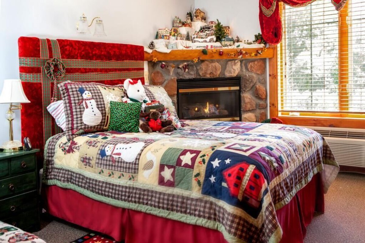 A cozy bedroom with a fireplace, a quilted bedspread, and a Christmas-themed headboard.
