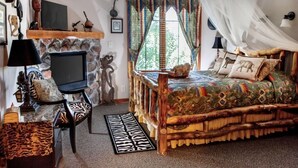 A cozy bedroom with a stone fireplace, a bed with a patterned bedspread, and a television on a wooden stand.