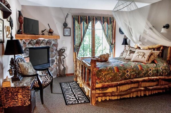A cozy bedroom with a stone fireplace, a bed with a patterned bedspread, and a television on a wooden stand. - The Lodge at Grant's Trail (St. Louis)