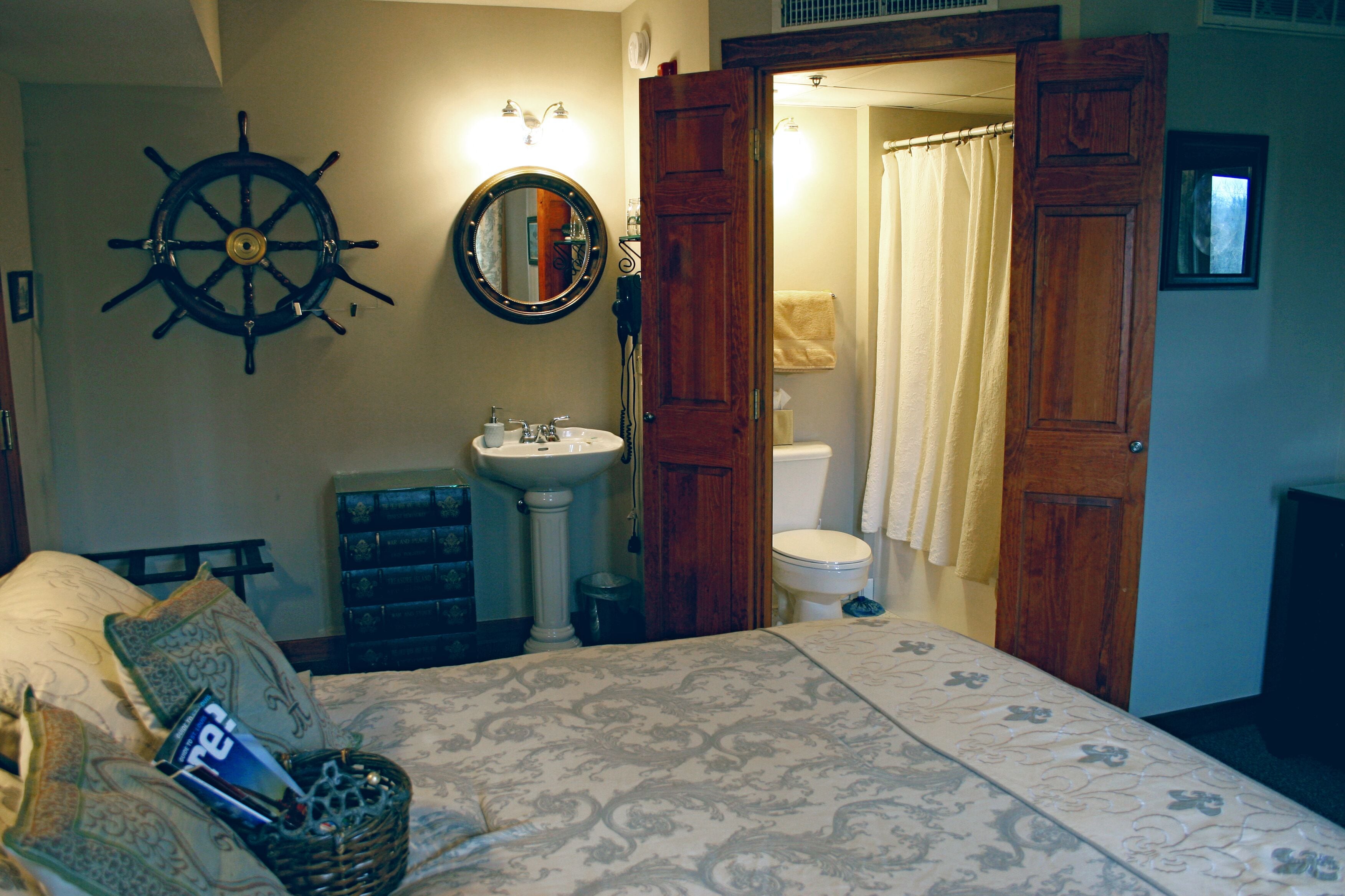 Un dormitorio con cama, puerta de madera, baño con lavamanos, inodoro y cortina de ducha.