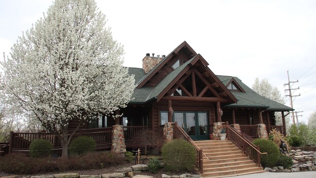 A log cabin with a stone chimney, wooden deck, and a staircase leading to the entrance.