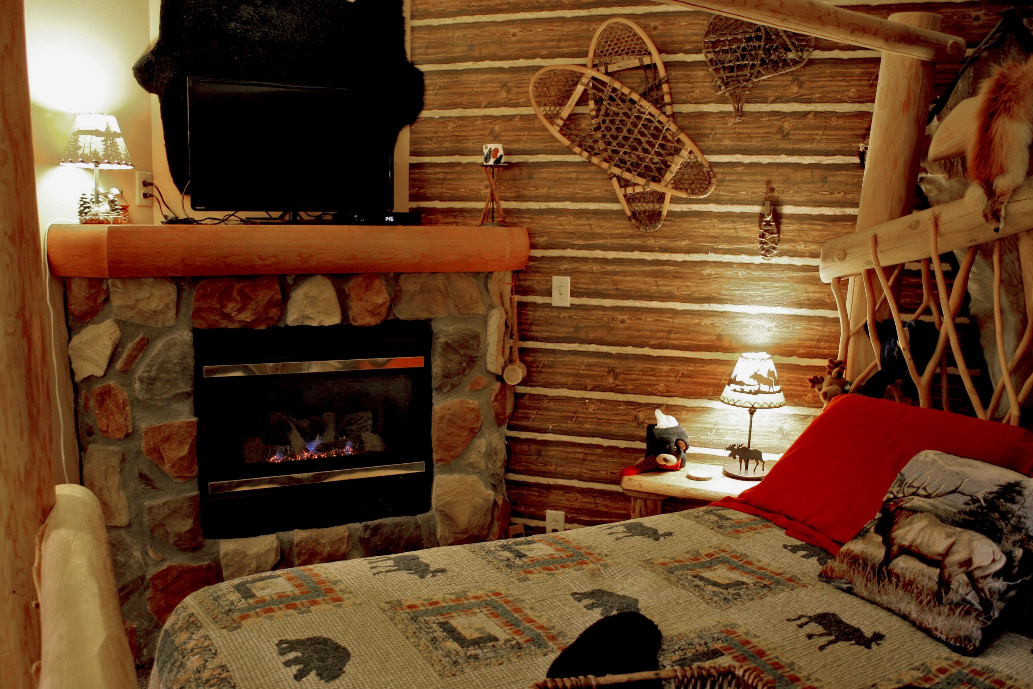 A cozy room with a stone fireplace, a television mounted on the wall, a woven basket, and a red pillow on the bed.