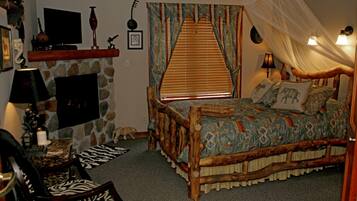 Un dormitorio con chimenea de piedra, una cama con colcha estampada, un sillón con estampado de cebra y un televisor montado en la pared.