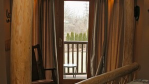 A rustic wooden bed with a quilt, a chair, and a view of the outdoors through a door.