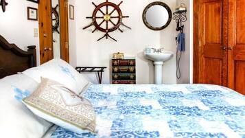 Una camera da letto con un letto, una porta in legno, una ruota di timone a muro, uno specchio, una libreria e un lavandino bianco.