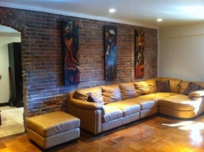 A living room with a brick wall, a large L-shaped sofa, and three abstract paintings. - Hemmerling House (Jackson)