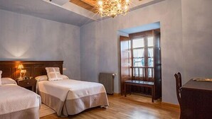 Habitación de hotel con dos camas, cabecera de madera, candelabro, ventana y una mesa.