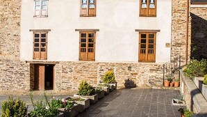 Un edificio de piedra con entrada central, varias ventanas y un patio empedrado con plantas en macetas.