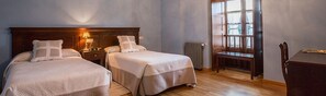 A hotel room with two beds, a nightstand with a lamp, a chair, and a window with blinds. - La Casona de Amaido (San Tirso de Abres)