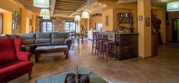 A spacious living area with a red sofa, a wooden bench, and a bar area with stools. - La Casona de Amaido (San Tirso de Abres)