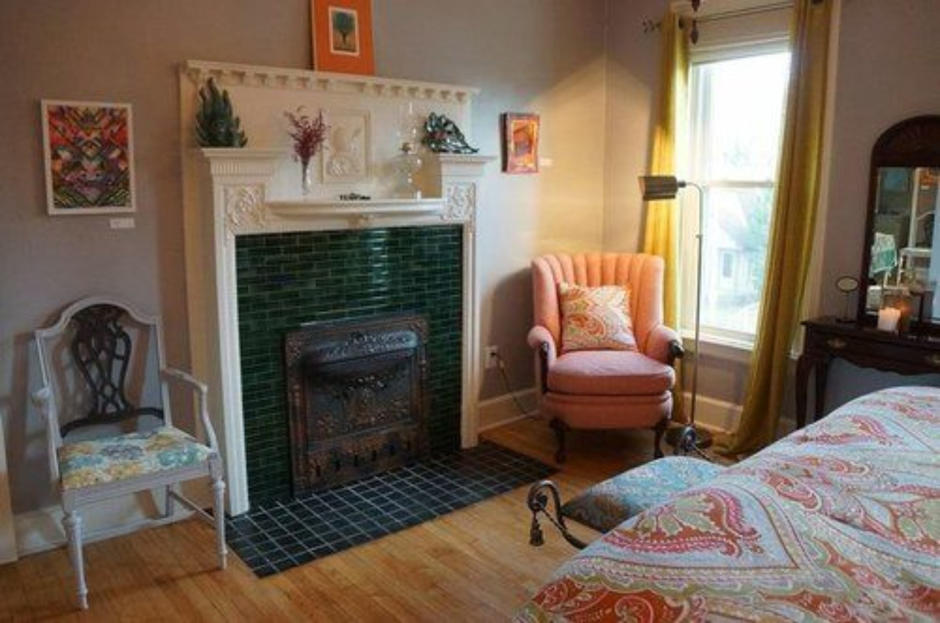 Una habitación con chimenea, una silla, una cama y una ventana con cortinas.