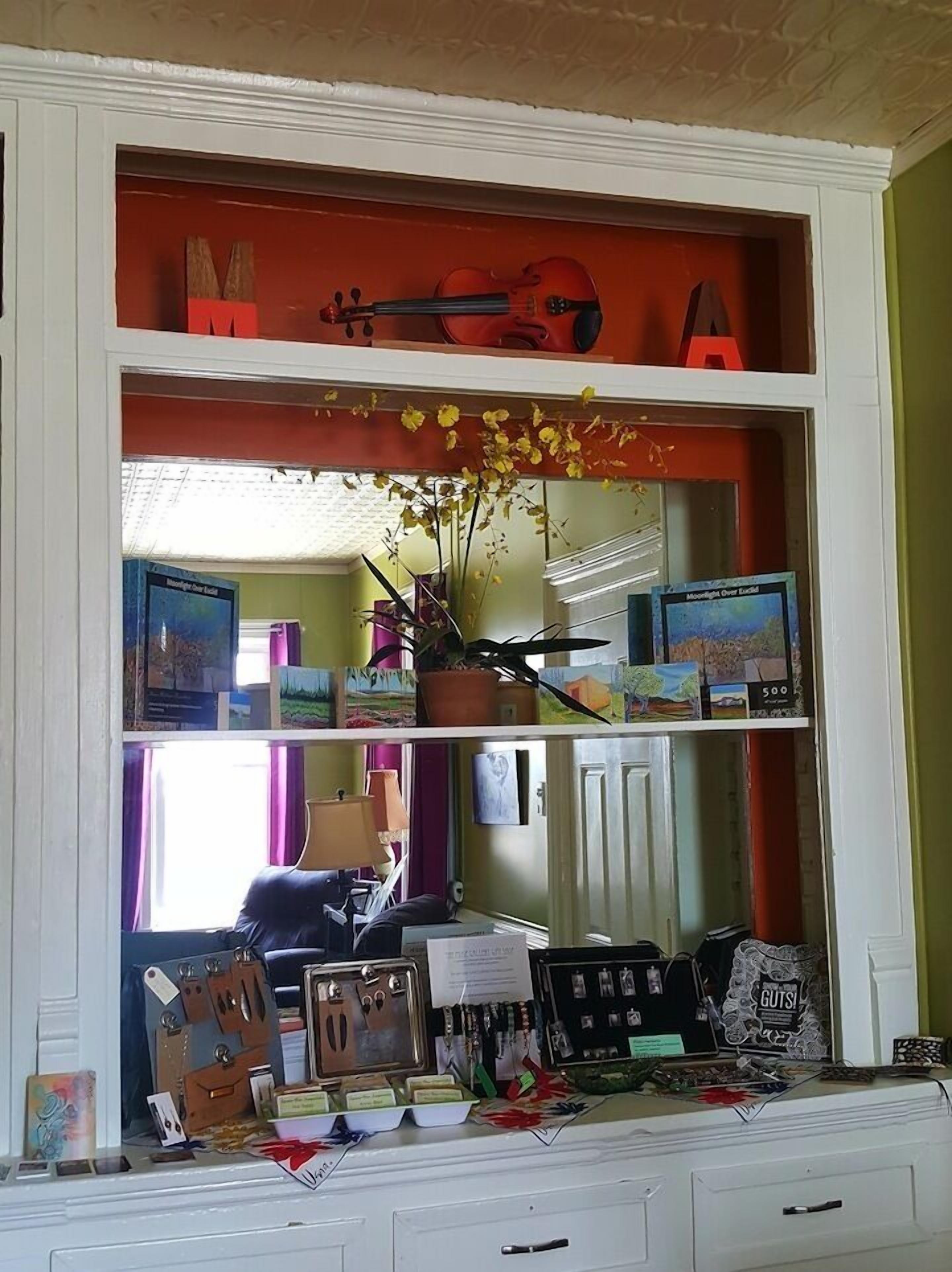 Una habitación con un armario blanco que exhibe varios objetos, incluyendo libros, un violín y elementos decorativos.