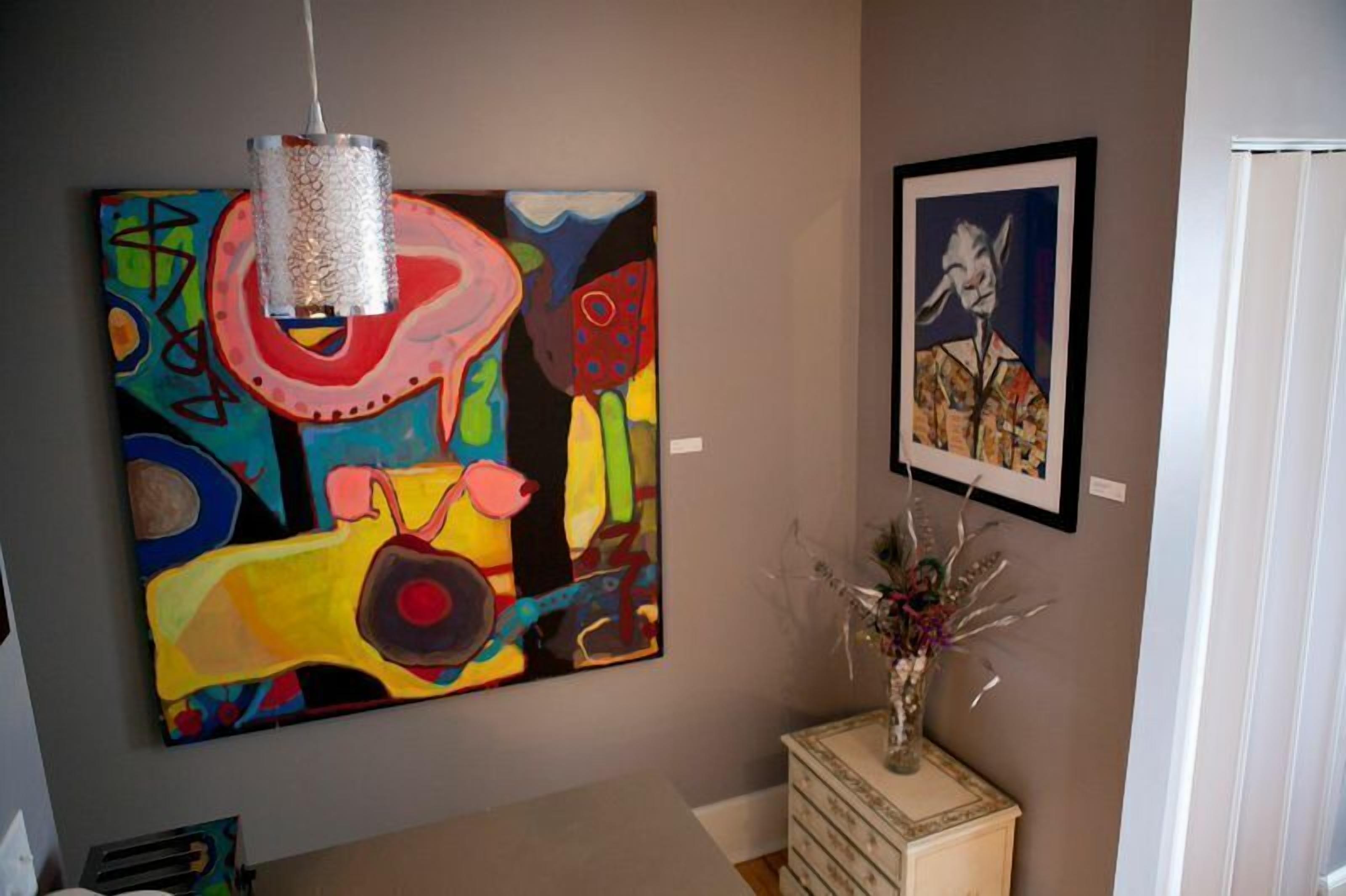 Een kamer met een kleurrijk abstract schilderij, een ingelijst portret en een decoratieve vaas.