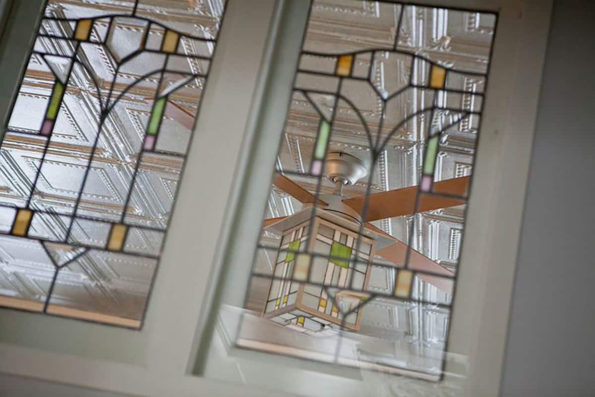 Un ventilateur de plafond dans une pièce dont les fenêtres sont ornées de vitraux.