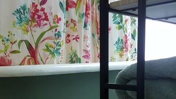 A bathroom with a green bathtub, floral curtains, and a shelf with folded towels.