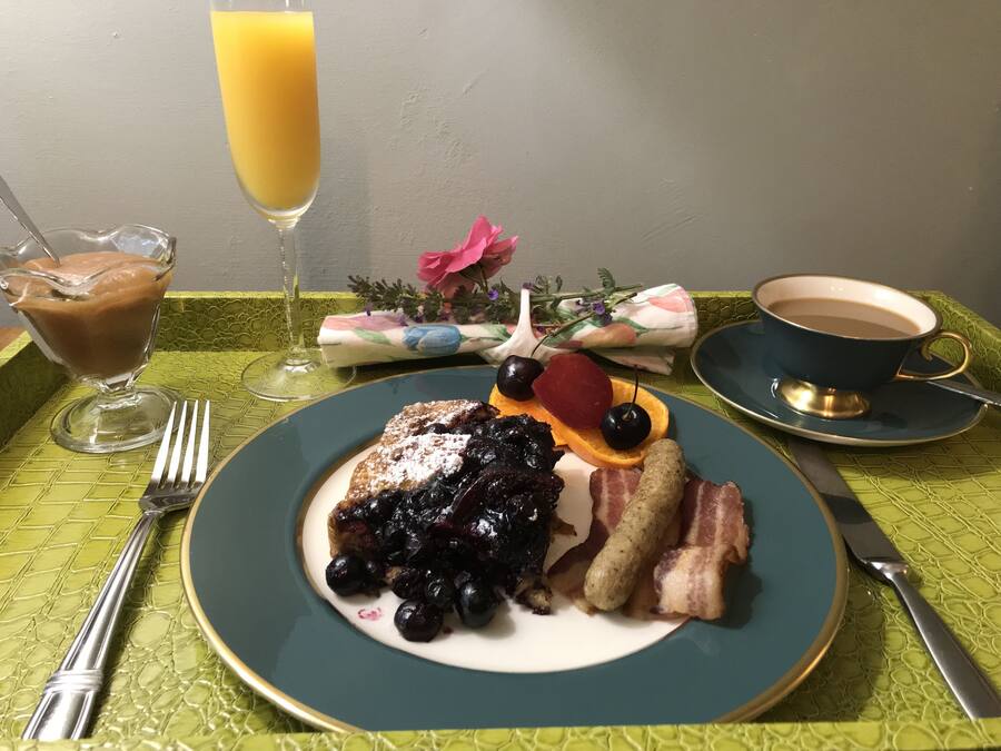 Ein Frühstücksteller mit Pfannkuchen, Blaubeeren, Speck und einem Glas Orangensaft.