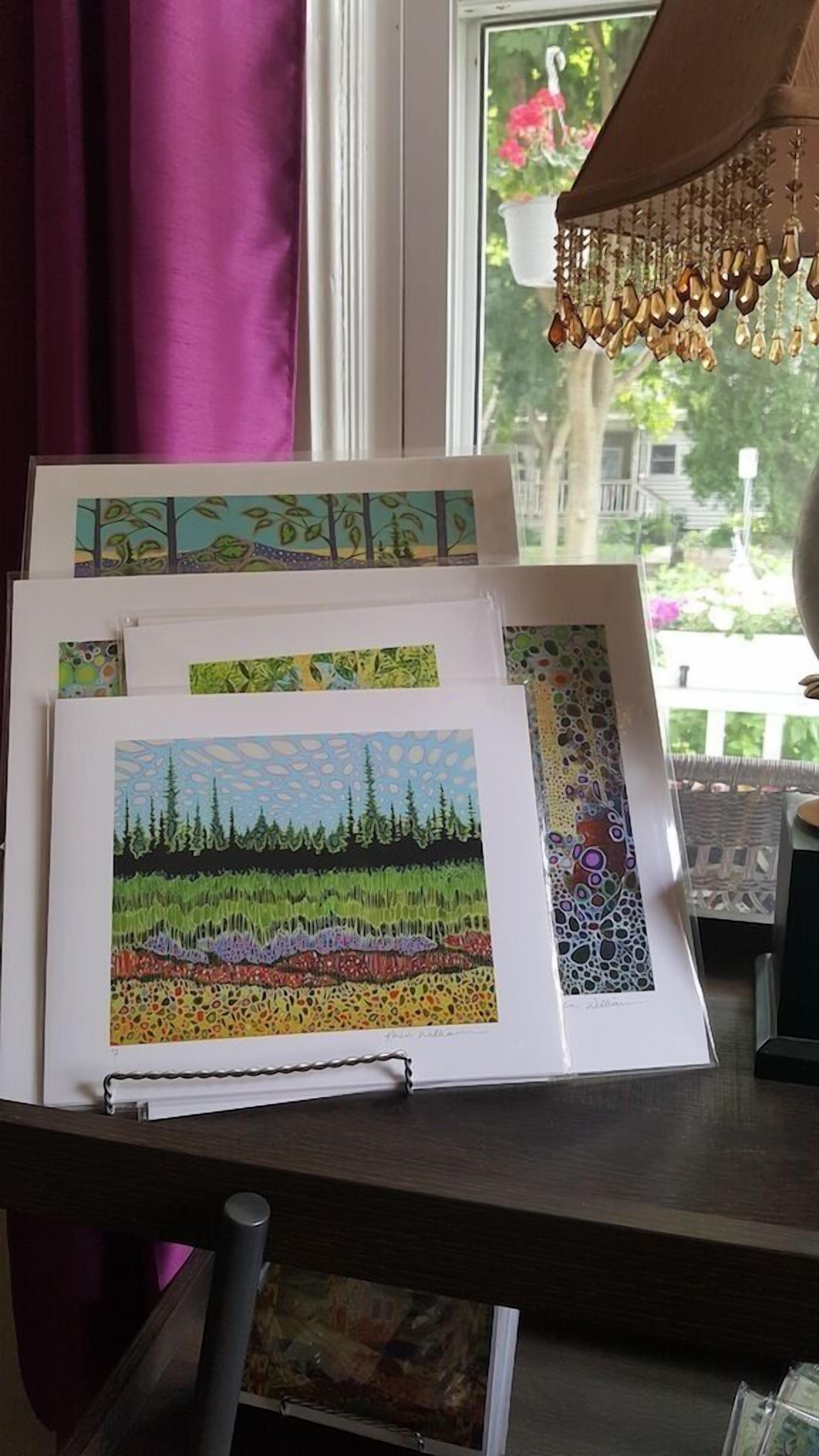 A framed artwork on a desk near a window with a view of a house and trees.