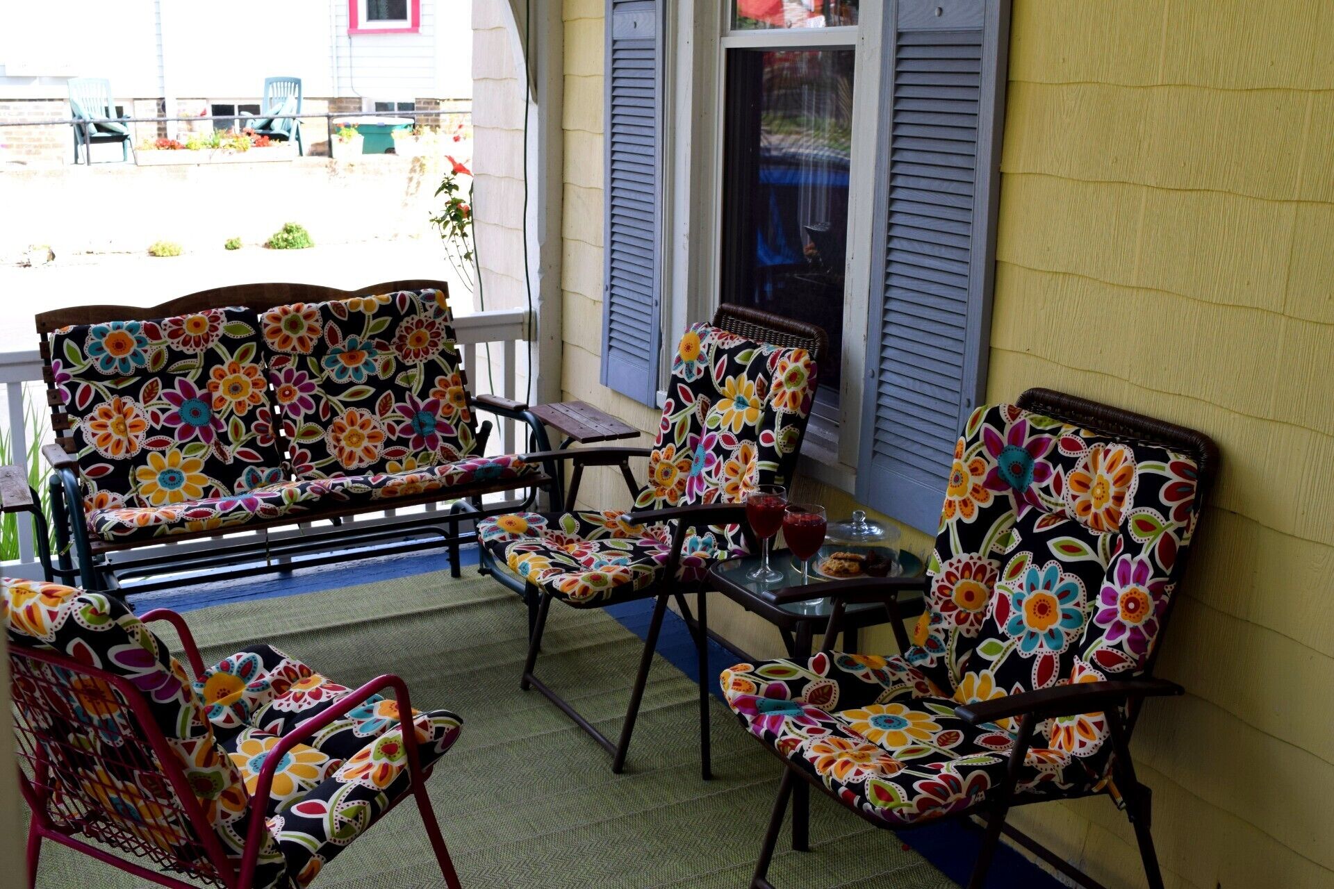 A porch with two chairs and a small table, featuring colorful floral upholstery.