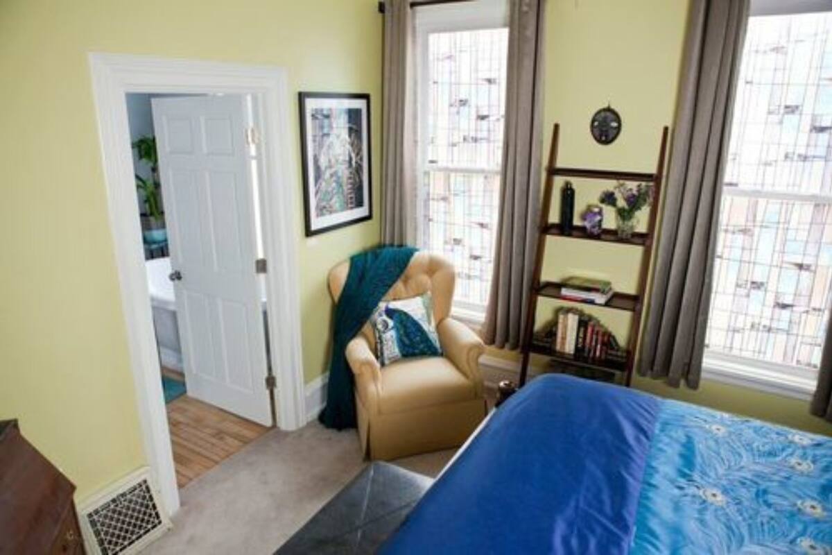Une chambre à coucher comprenant un lit, une chaise, une bibliothèque et une porte donnant sur une autre pièce.
