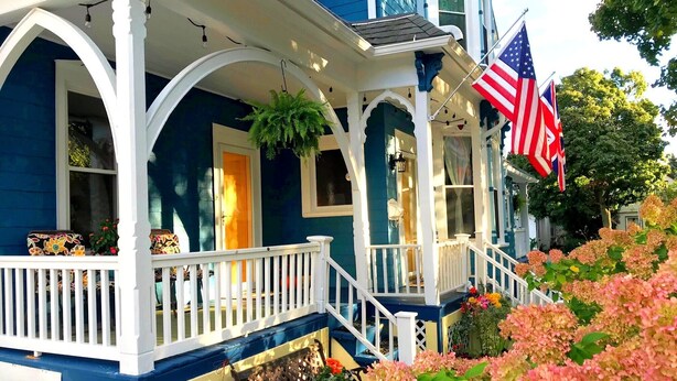 A blue house with a porch, white railings, and American flags. - The Muse Gallery Guesthouse (Milwaukee)