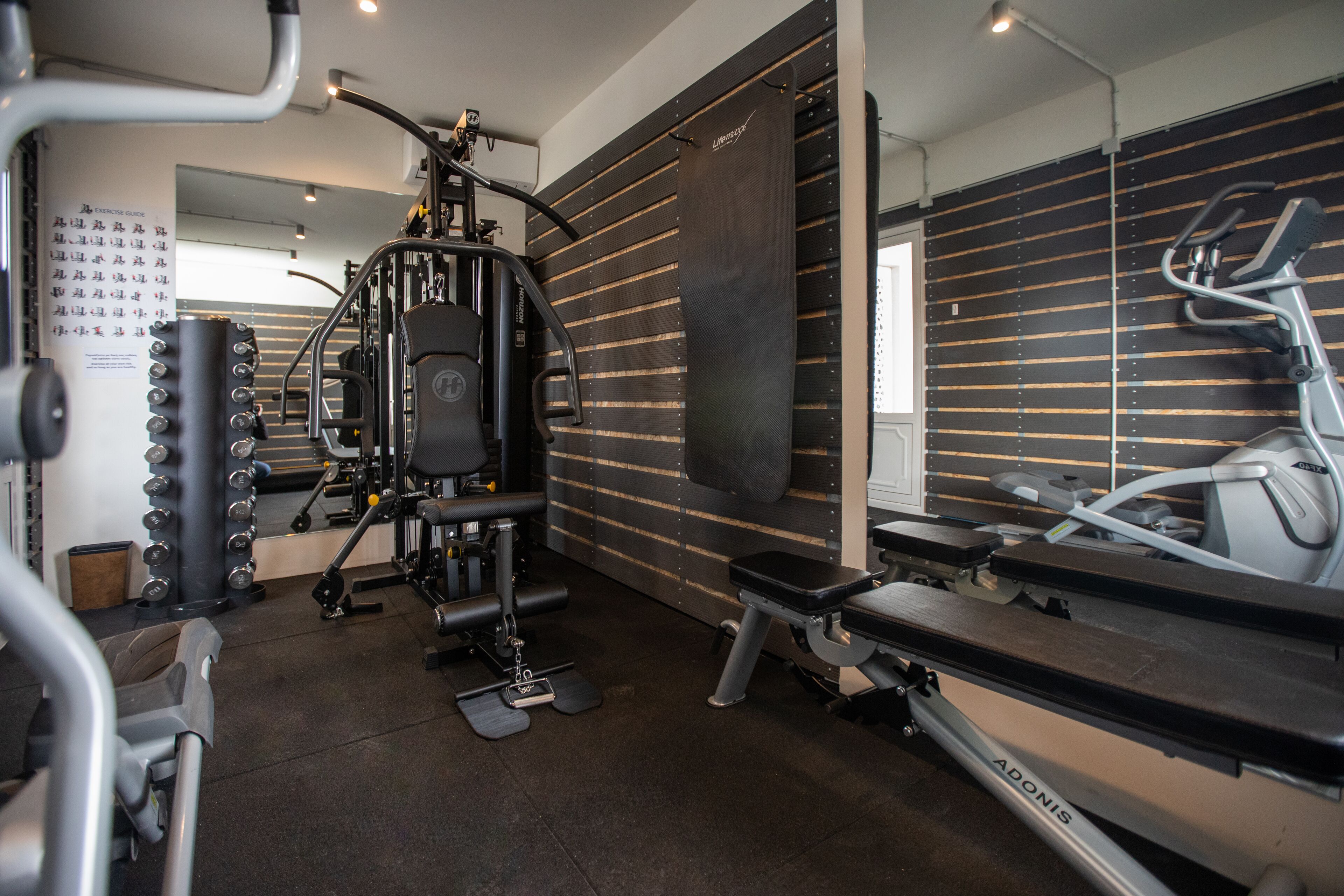 Een sportschool met diverse fitnessapparaten, waaronder een loopband, krachttoestellen en een bank.