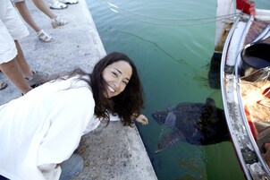 Una persona se inclina sobre el borde de un bote, observando una tortuga marina en el agua.