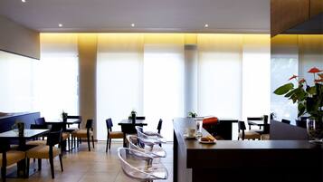 Un restaurante moderno con mesas altas, sillas transparentes, ventanas amplias y una cálida luz en el techo.