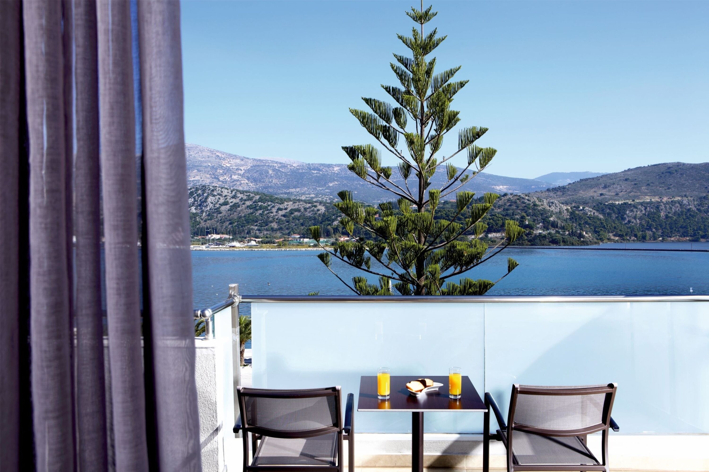Ein Balkon mit zwei Stühlen und einem Tisch, mit Blick auf einen See und Berge.