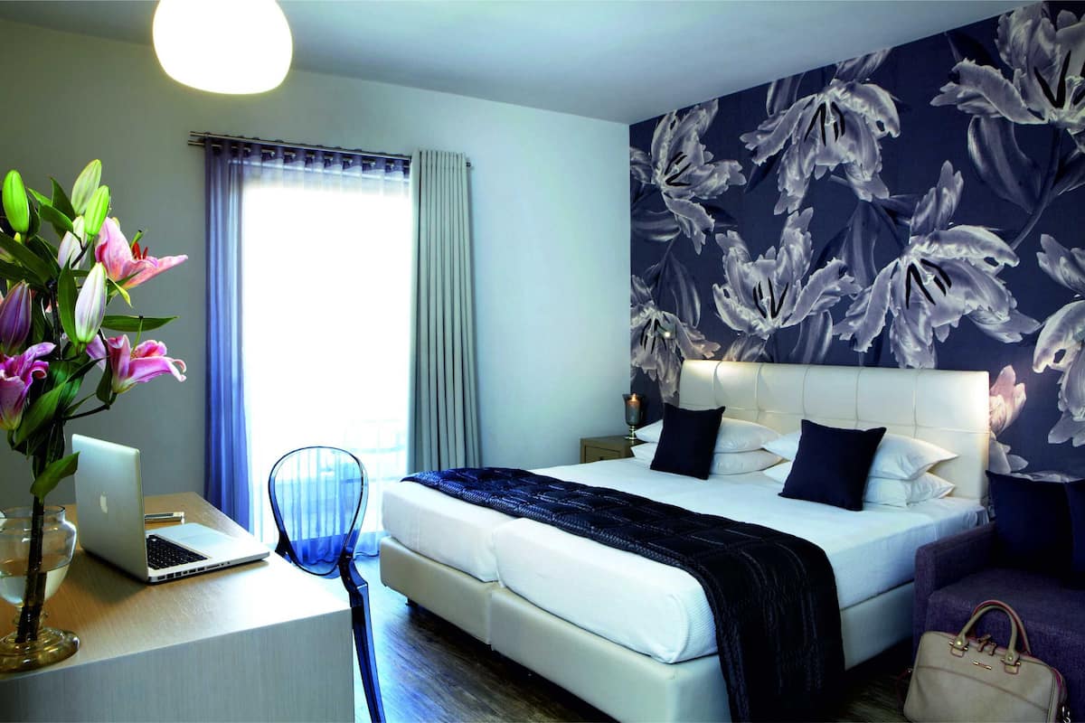 Een moderne hotelkamer met een groot bed, een bureau met een laptop, een bloemenvaas en een wand met een bloemendecoratie.