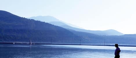 A person standing by a calm body of water with mountains in the background.
