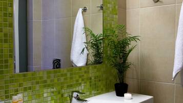 A bathroom with a green-tiled wall, a white sink, a mirror, a potted plant, and two towels.