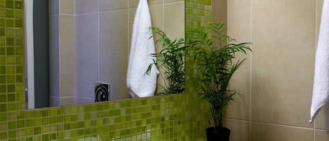 A bathroom with a green-tiled wall, a white sink, a mirror, a potted plant, and two towels.