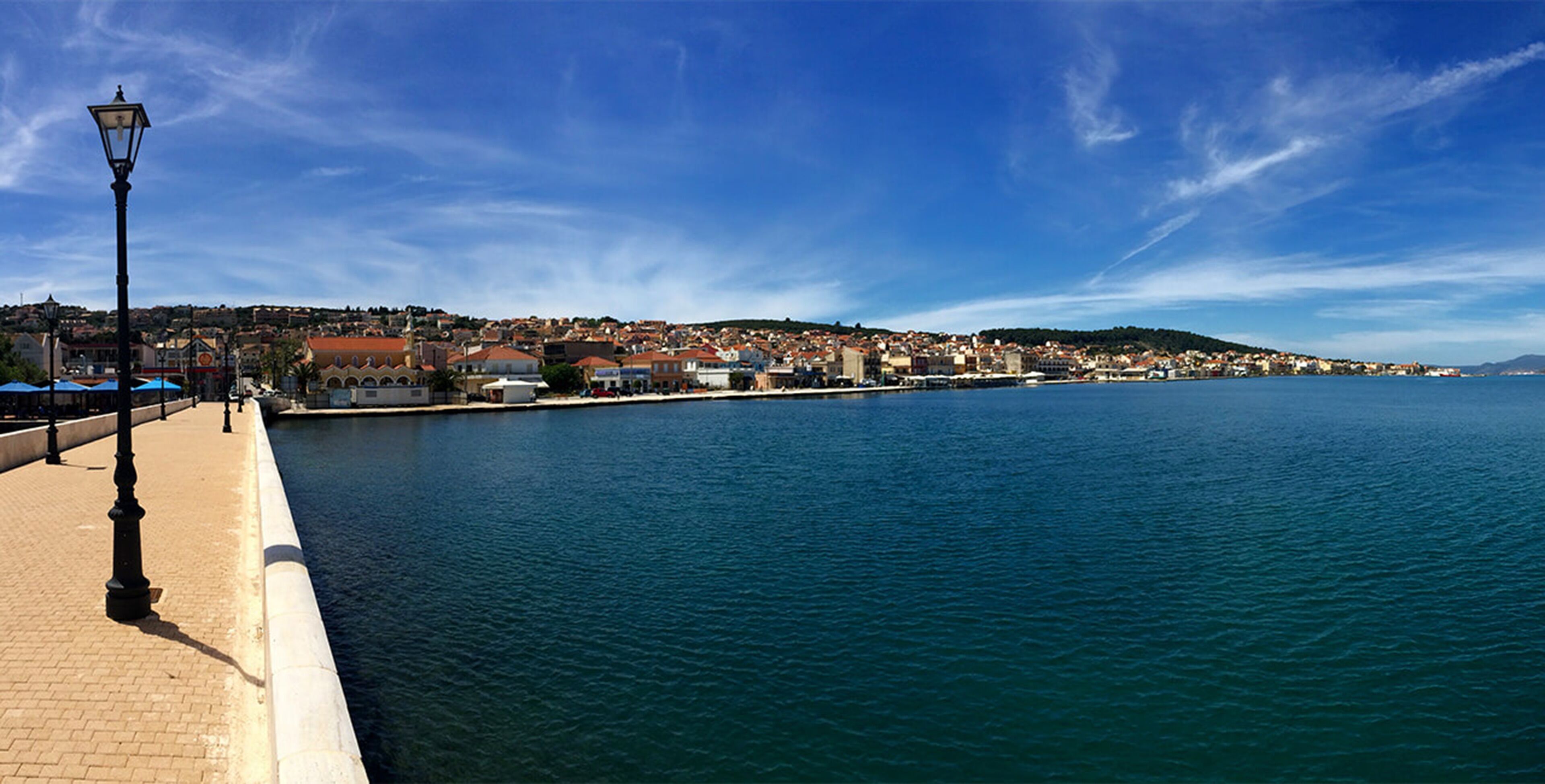 A waterfront promenade with a paved walkway, a lamp post, and buildings along the shore.