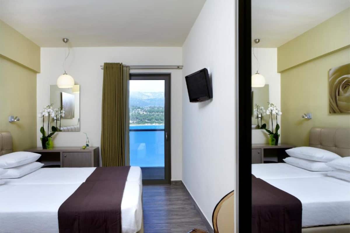 Een hotelkamer met twee bedden, een televisie, een balkon met uitzicht en een spiegel.