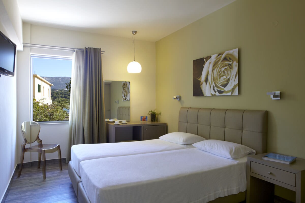 Ein Hotelzimmer mit Bett, Schreibtisch, Stuhl, einem Fenster mit Vorhängen, einem Gemälde und Blick nach draußen.