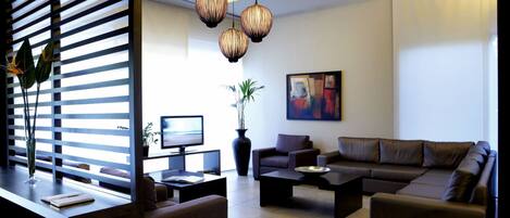 Una sala de estar moderna con un conjunto de sofás, una mesa de centro, un televisor y un ventanal con persianas.