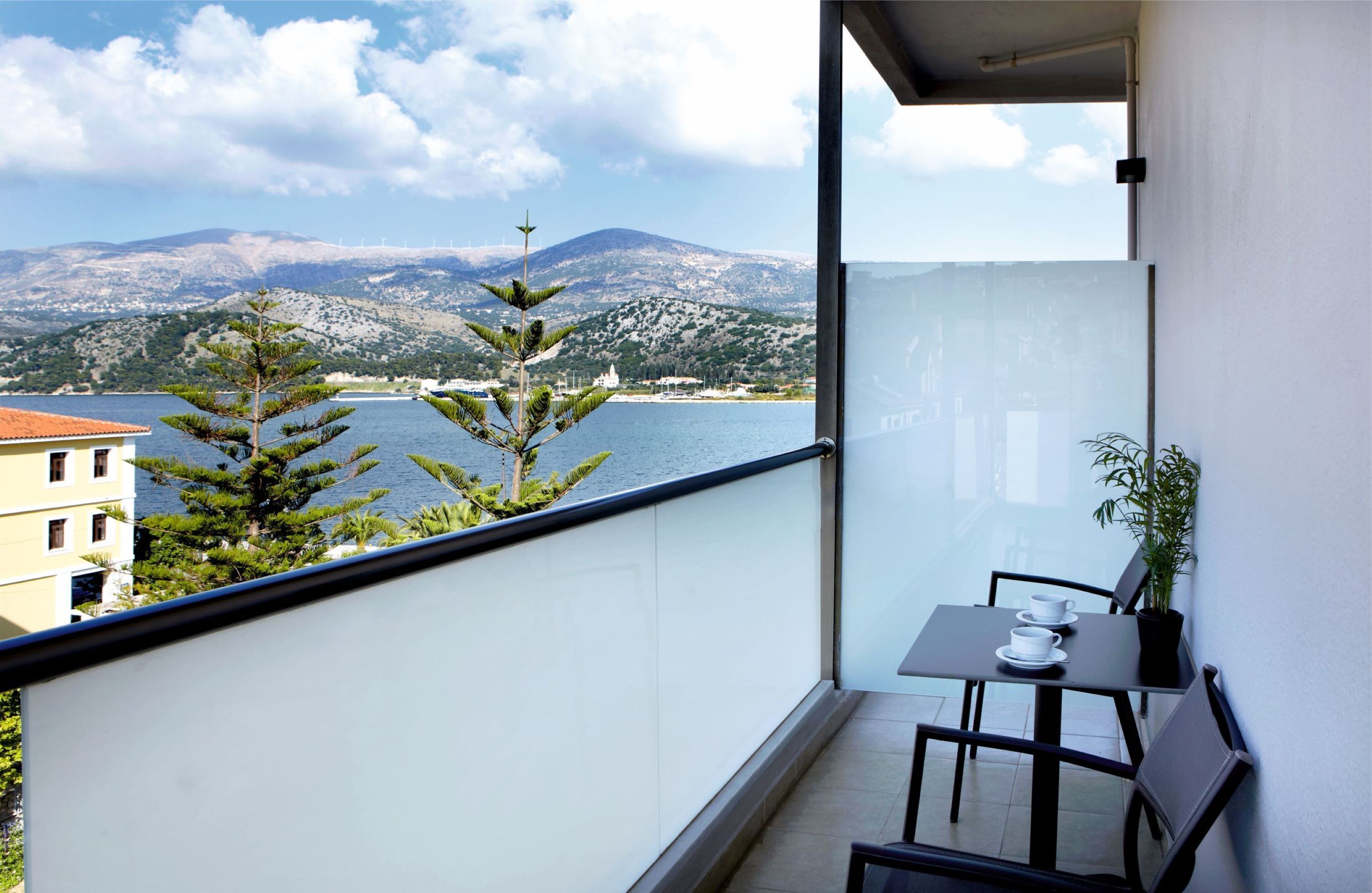 A balcony with a table and chairs, overlooking a body of water and mountains.