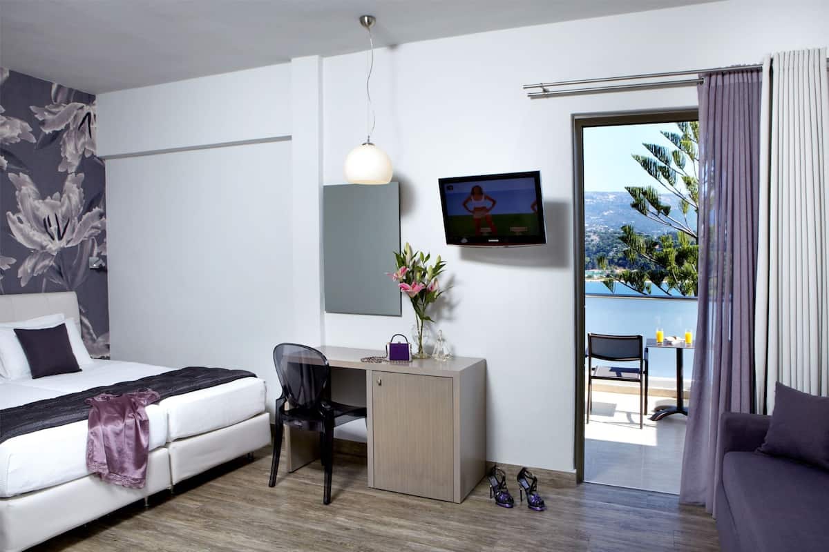 Een moderne hotelkamer met een bed, bureau, stoel, televisie en een balkon met uitzicht.