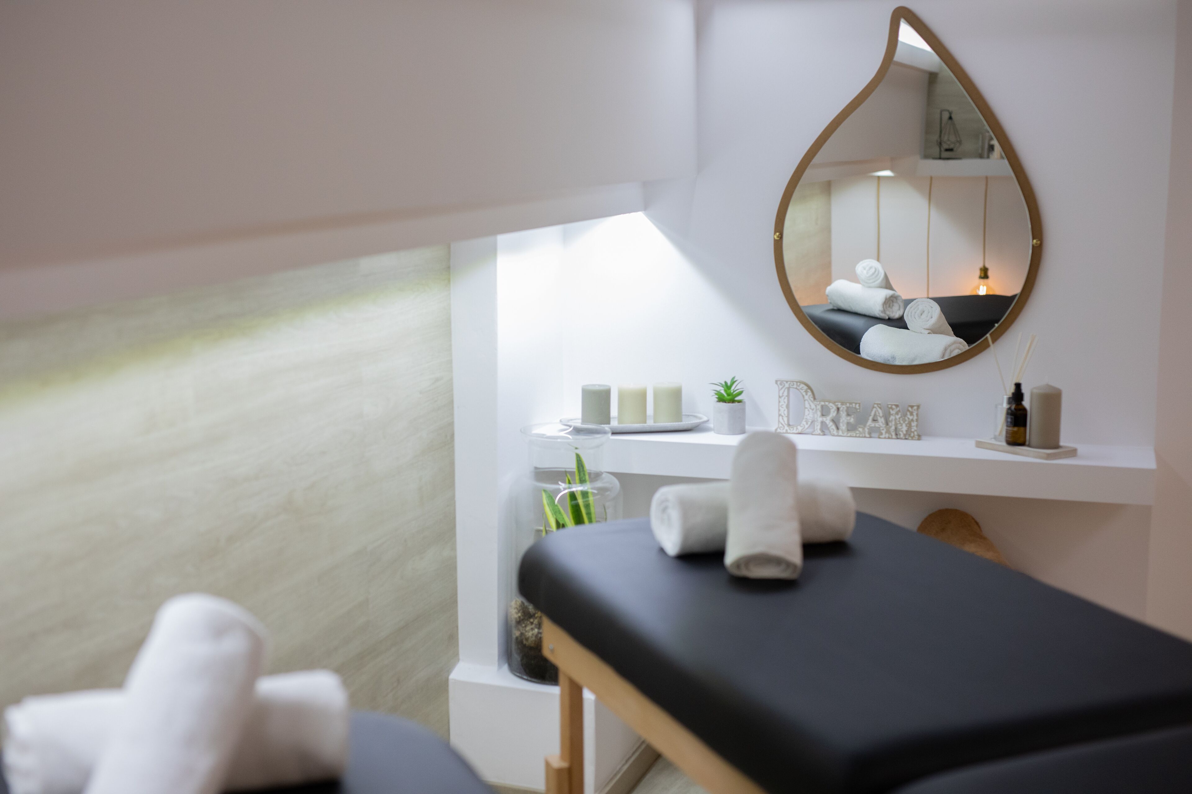 Un cuarto de spa con una camilla de masaje, un espejo, un estante con toallas y velas, y una ventana con vistas.
