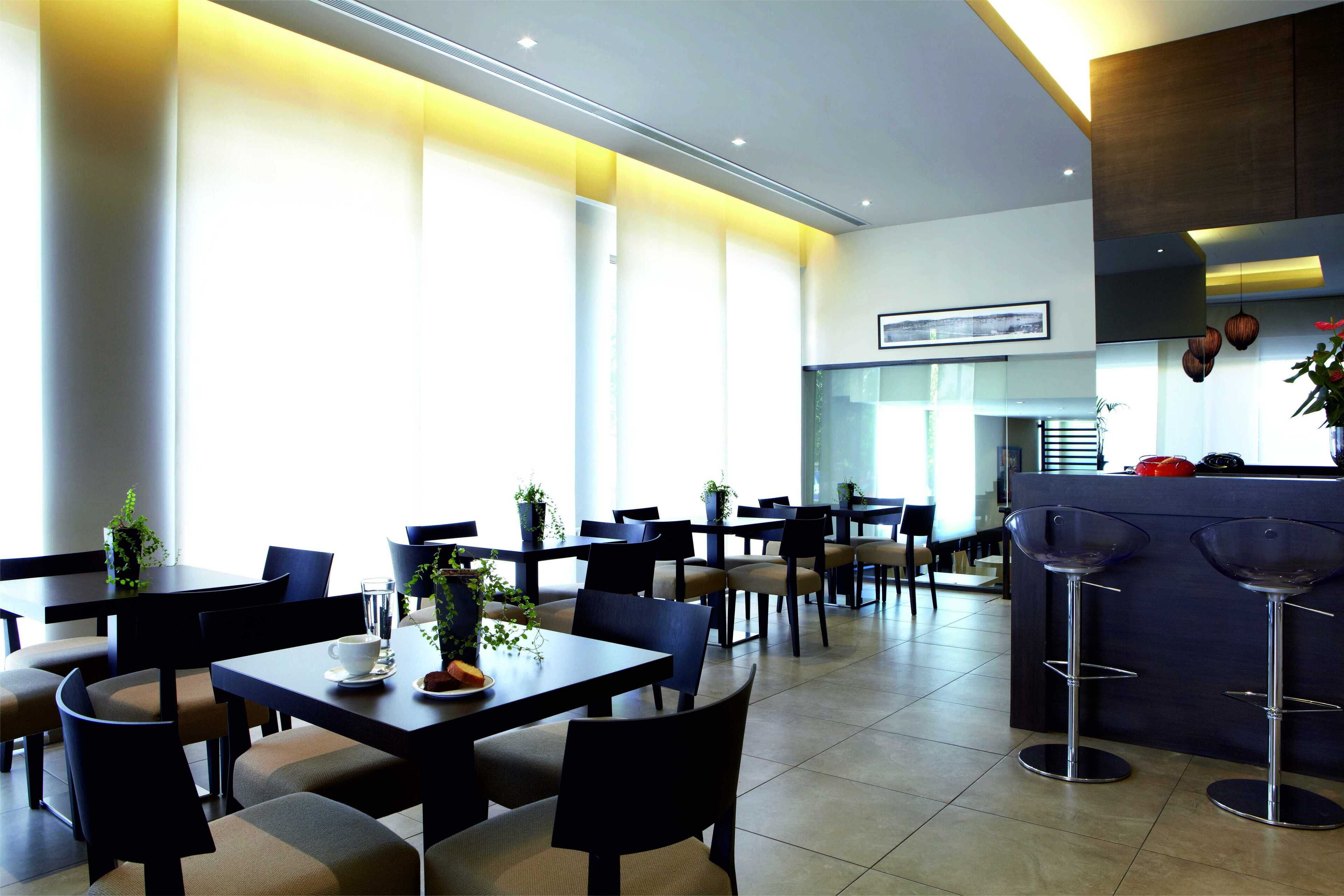 Un restaurante moderno con varias mesas y sillas, ventanas amplias y una zona de bar.