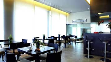 Un restaurante moderno con varias mesas y sillas, ventanas amplias y una zona de bar.